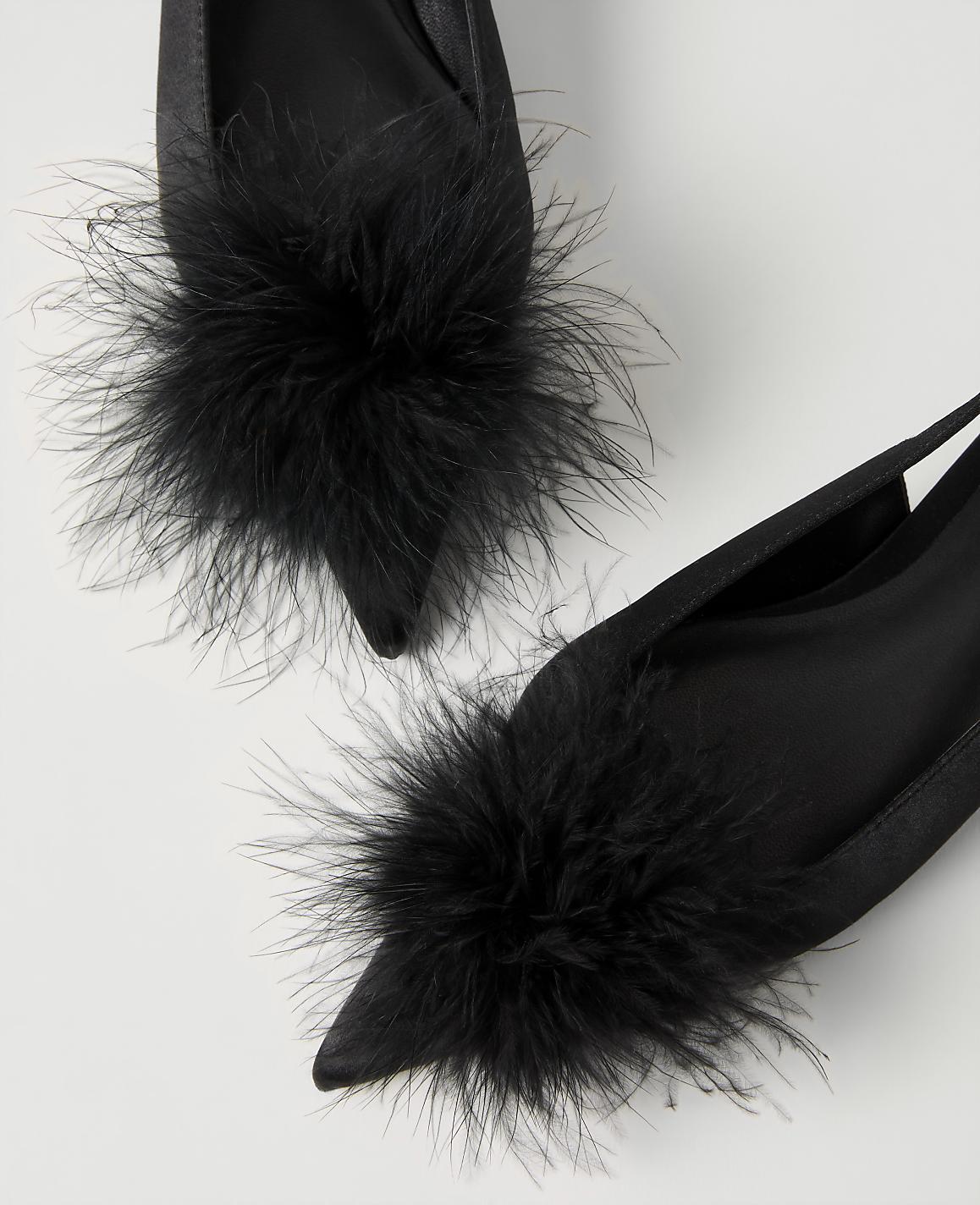 Two black satin pointed-toe shoes with fluffy black feather pom-poms are set against a plain white background.