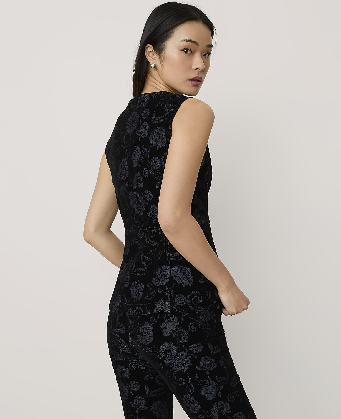 A woman wearing a black floral velvet two-piece set poses against a plain, light-colored background.