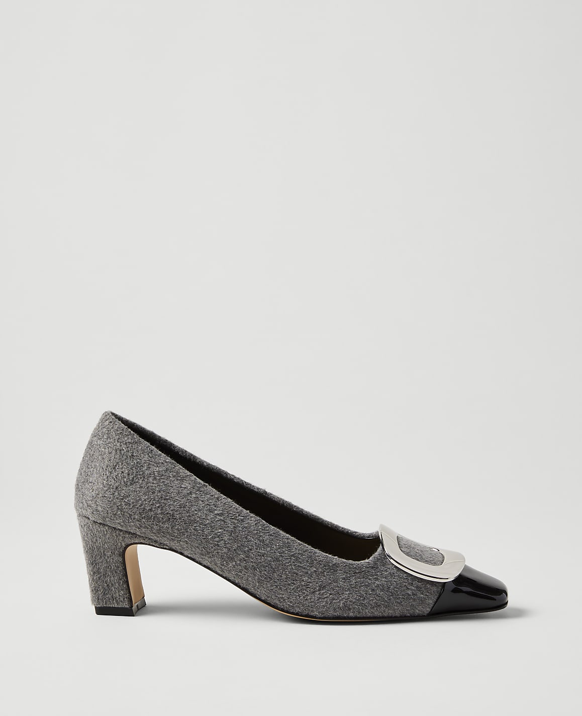 A grey felt pump with a black patent leather toe cap and silver buckle sits against a plain light grey background.