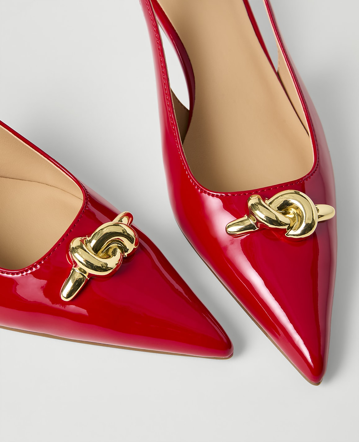 Two red patent leather pointed-toe slingback heels with gold chain ornaments rest on a plain white background.