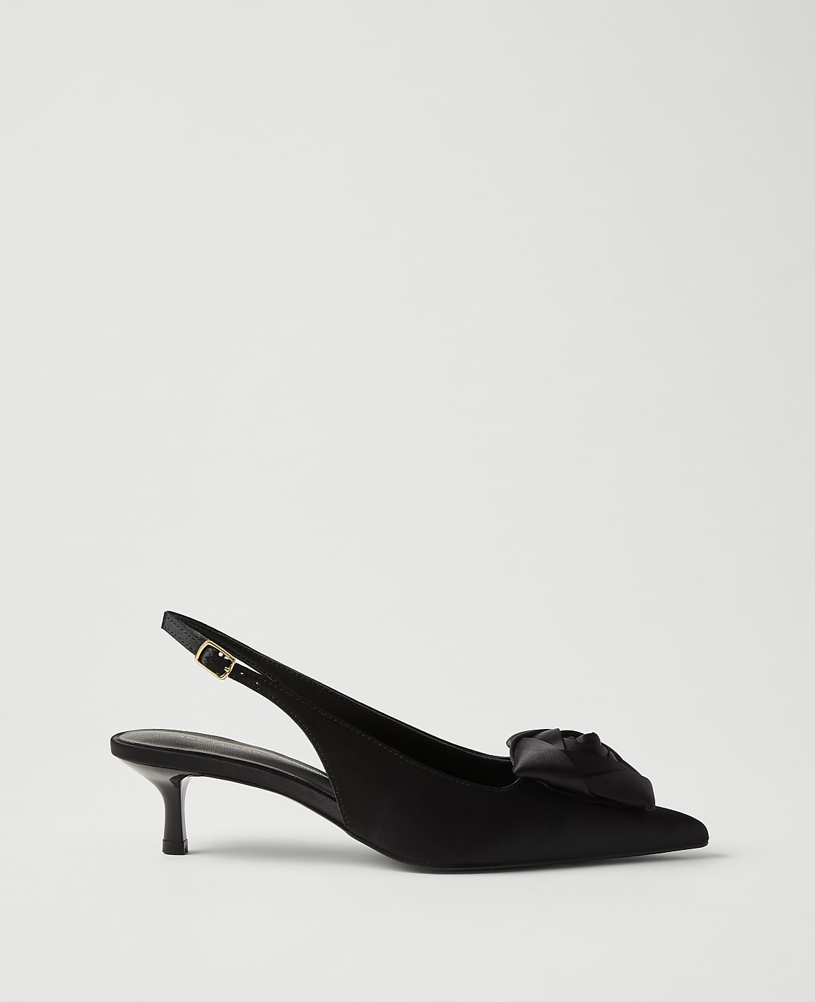 A black satin slingback heel with a decorative bow sits in the foreground against a plain, light gray background.