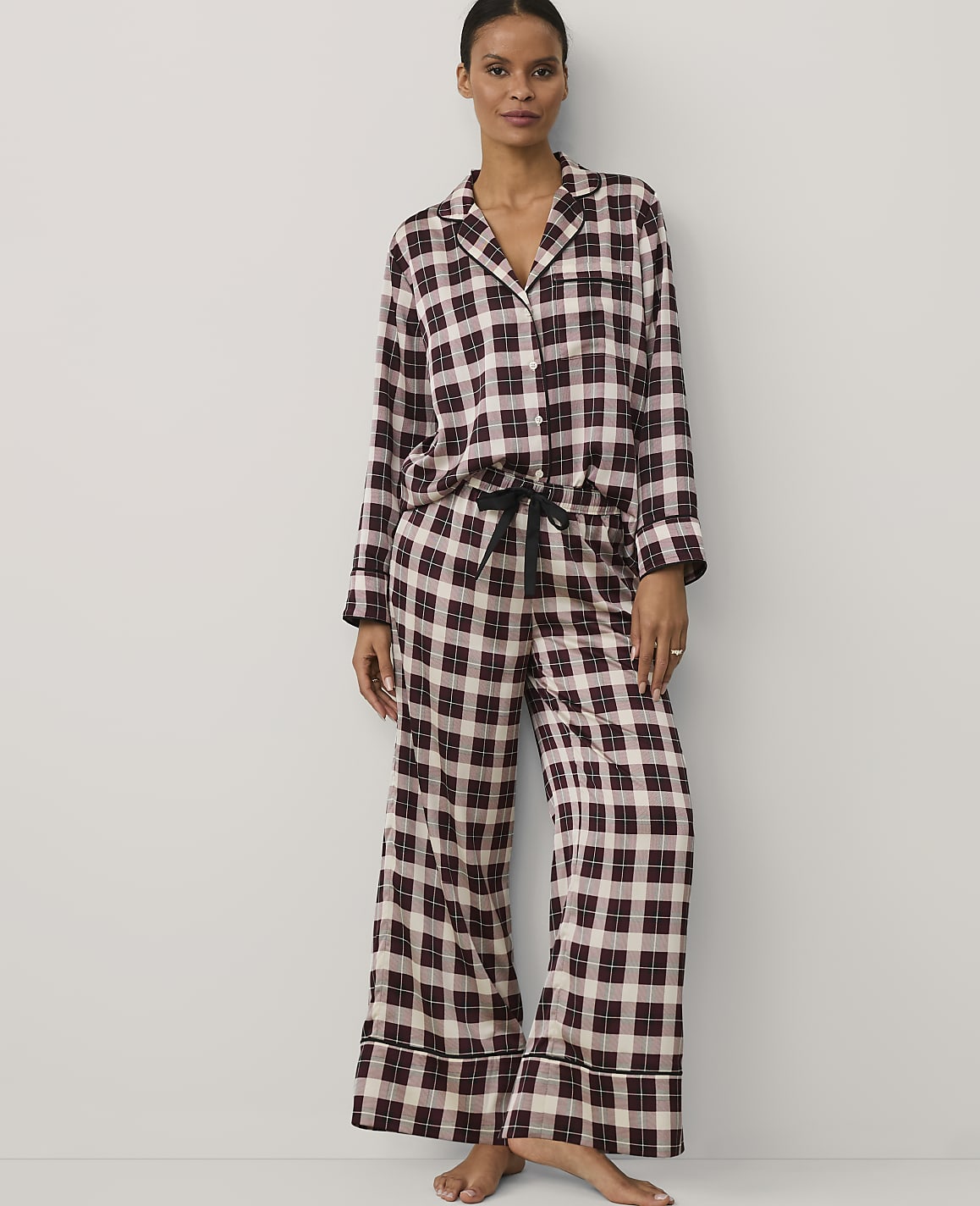 A woman wearing burgundy and white checkered pajamas stands against a plain white background.