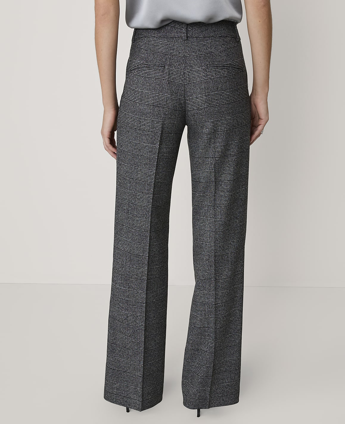 A person wears grey plaid wide-leg trousers and a silver top against a plain, light-colored background.