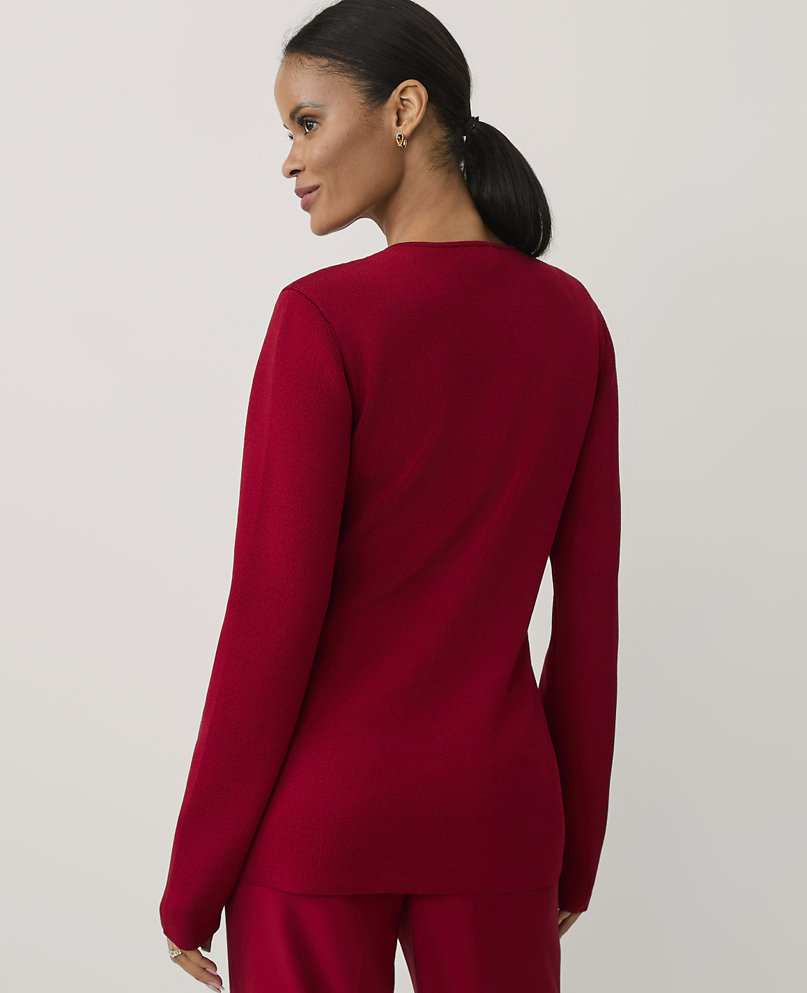 A woman wearing a red long-sleeved top and matching pants stands against a plain, light-colored background.