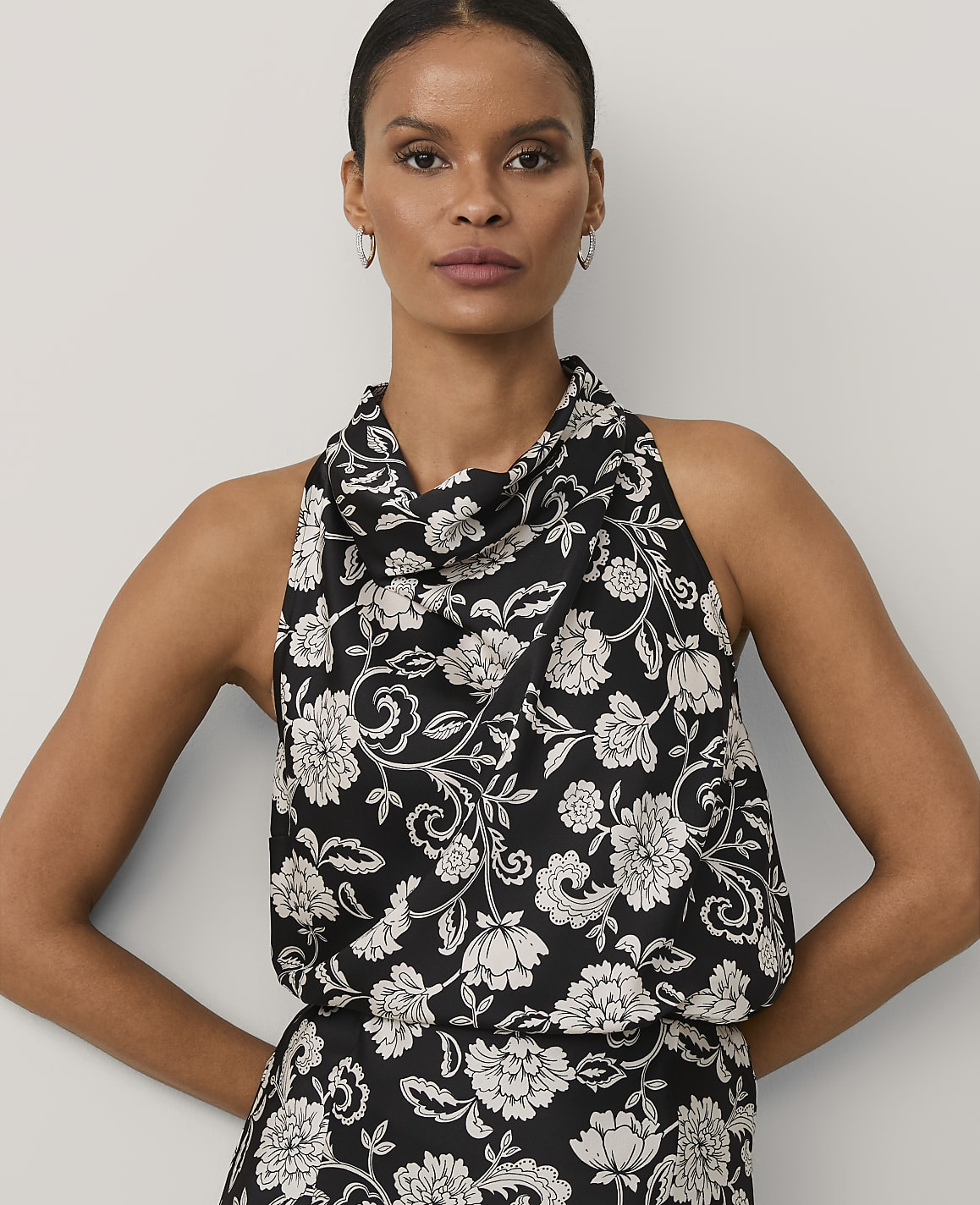 A woman wearing a black and white floral print halter dress stands against a plain light gray background.