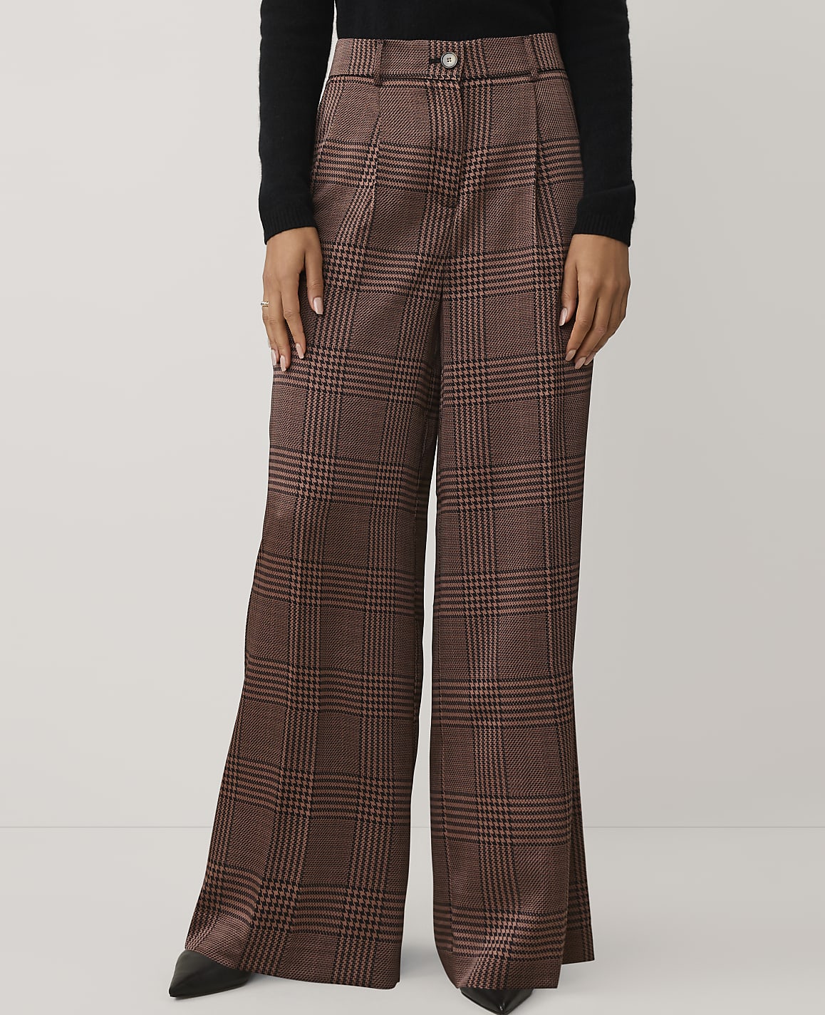 A person wears brown plaid wide-leg trousers and a black top against a plain white background.