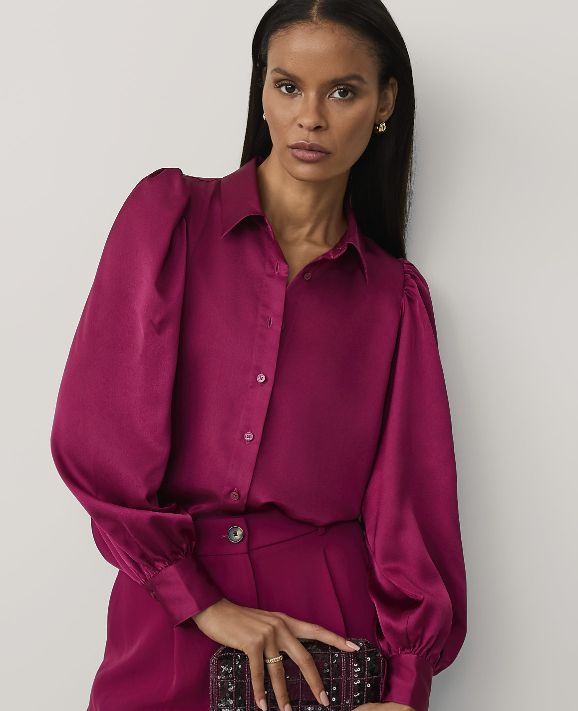 A woman wearing a magenta satin blouse and matching trousers stands against a plain white background.