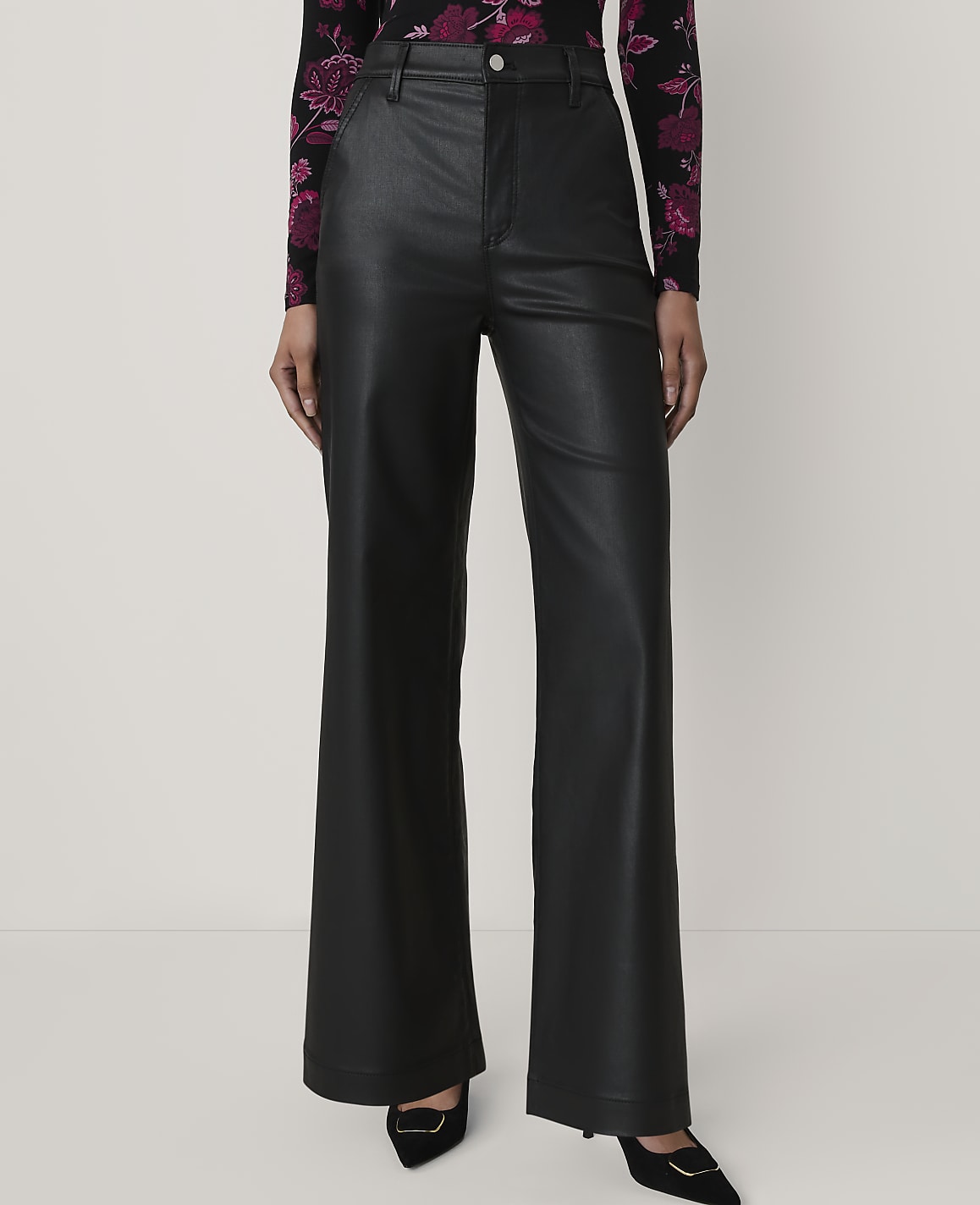 A person wears black faux-leather wide-leg trousers and a floral top against a plain white background.