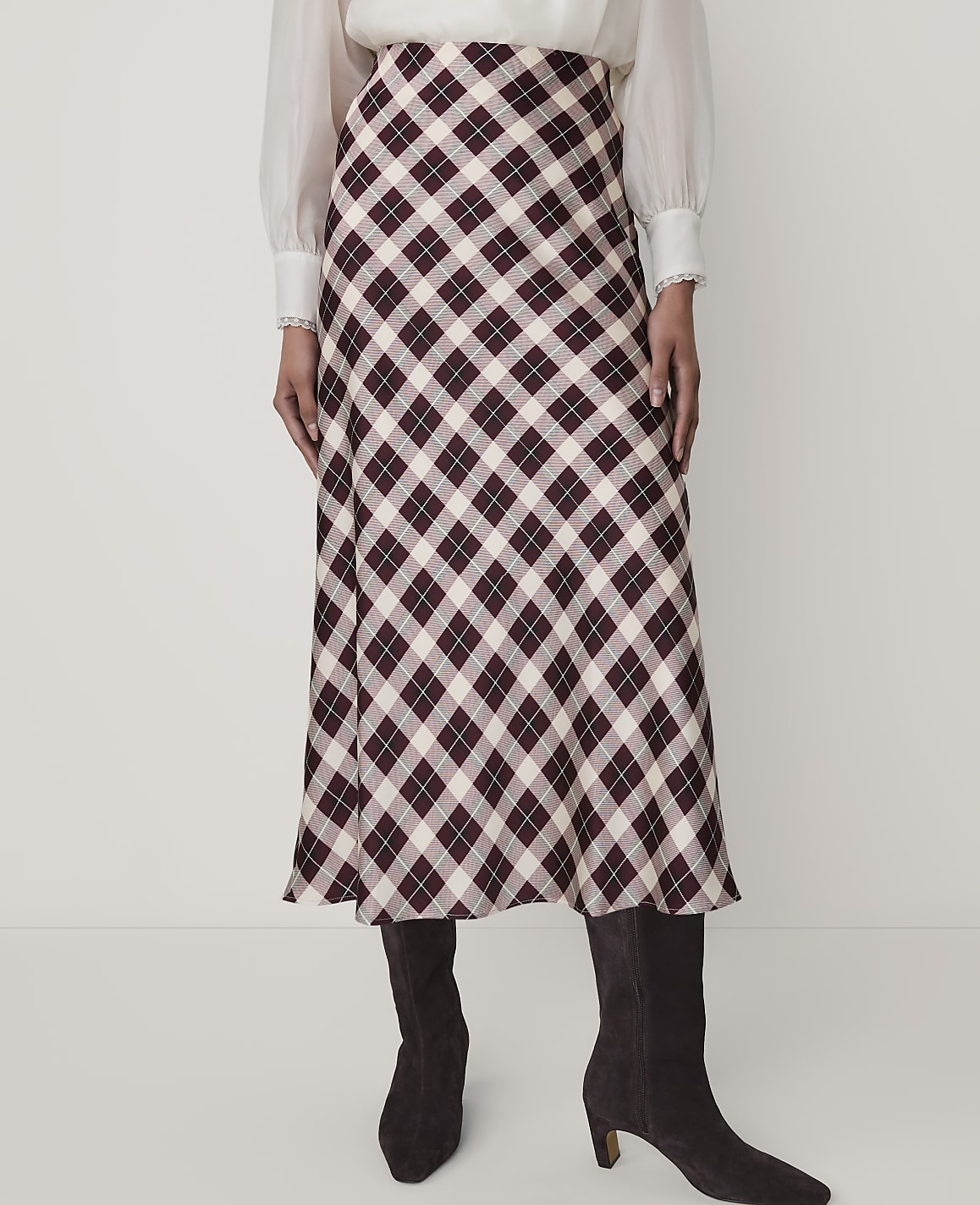 A person wears a white blouse, a burgundy and white plaid midi skirt, and dark brown boots against a plain white background.