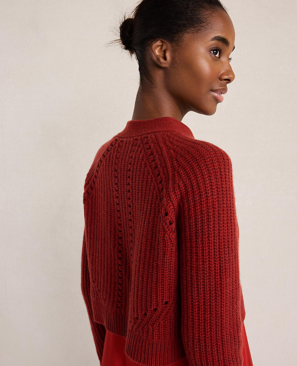 A woman with her hair in a bun wears a red knit sweater against a plain, light-colored background.