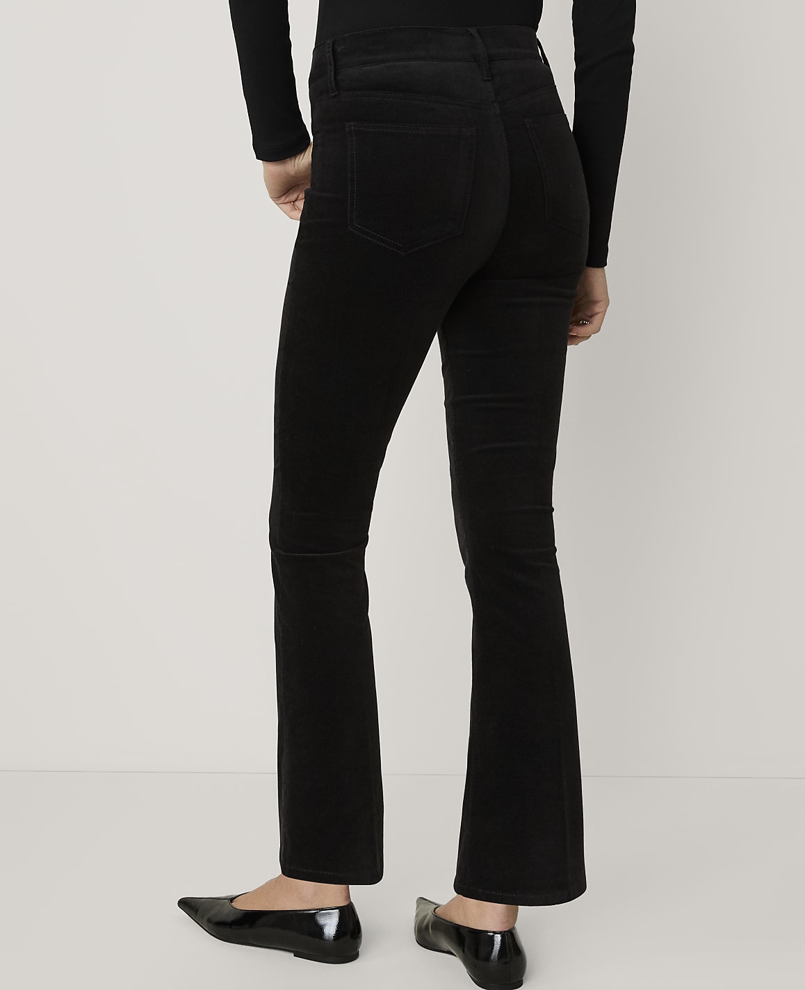 A person wearing black flared trousers and black flats stands against a plain white background.