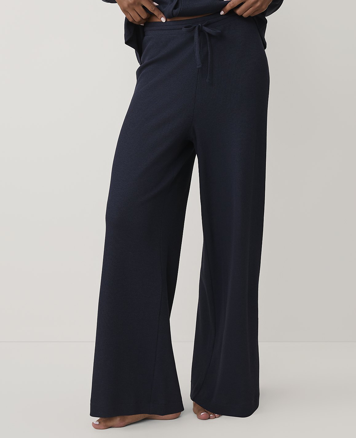 A person wears navy blue wide-leg ribbed trousers against a plain, light-colored background.