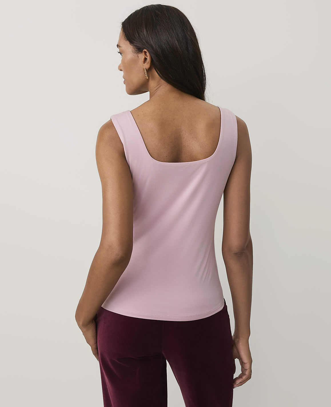 A woman wearing a light pink sleeveless top and maroon velvet pants stands against a plain, light-colored background.