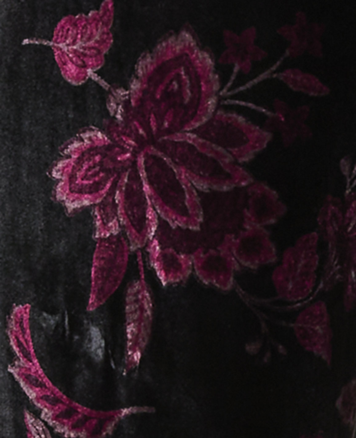 Intricate magenta floral embroidery is stitched onto a dark black velvet background.