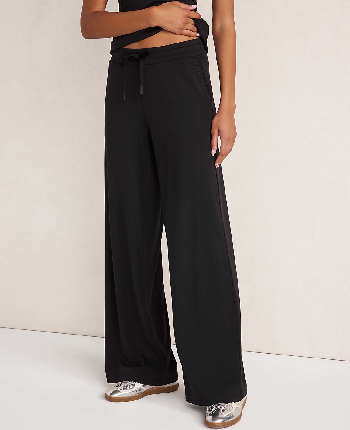 A person wears wide-leg burgundy trousers and a matching top against a plain, neutral-toned wall.