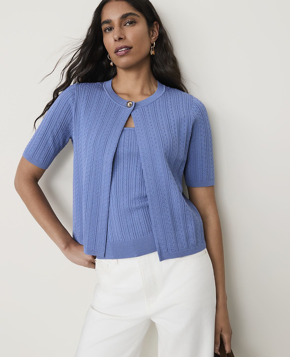 A woman in a blue cardigan and matching top stands against a plain, light-colored background.