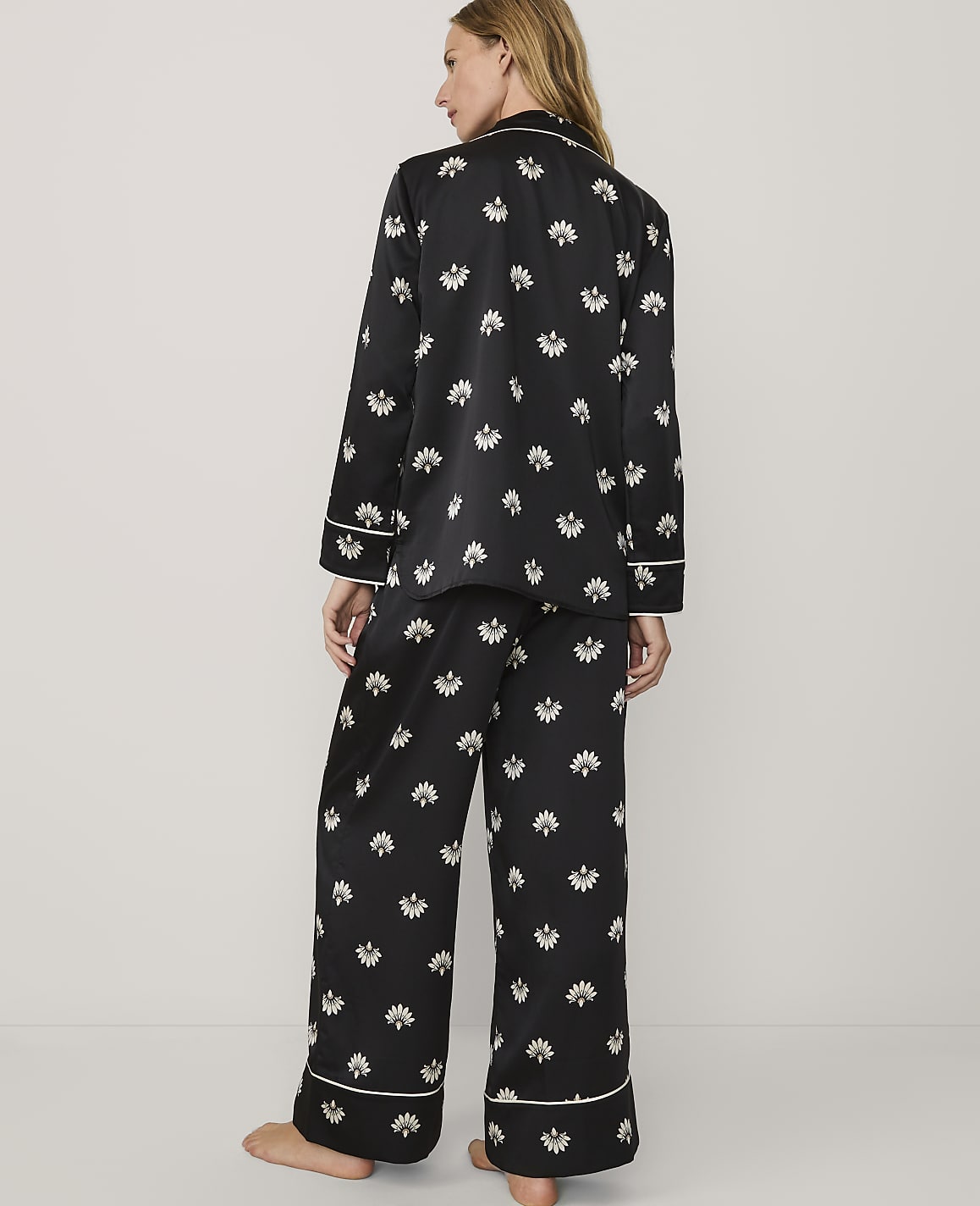 A woman stands with her back to the camera wearing black floral pajamas against a plain white background.