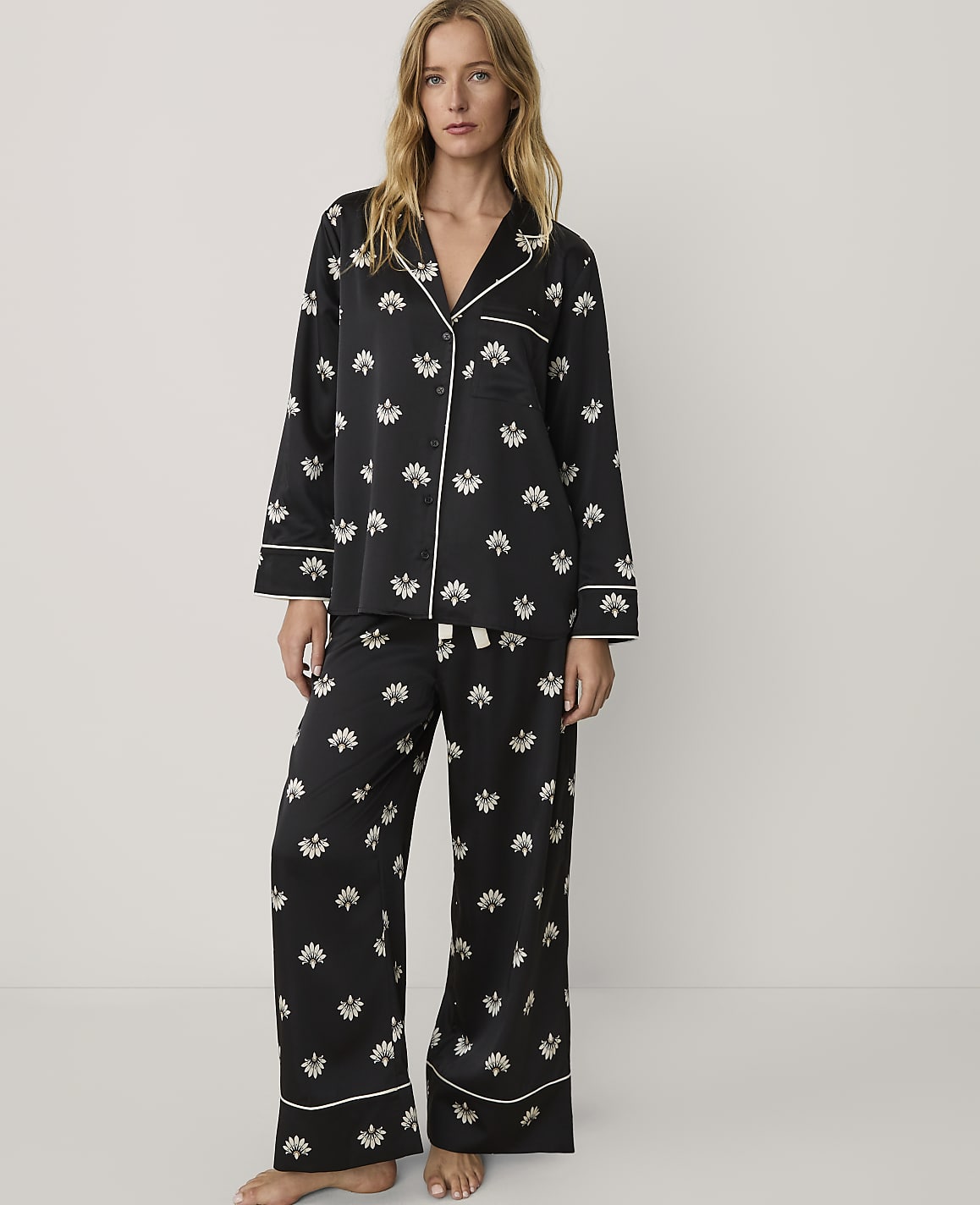 A woman wearing black floral pajamas stands against a plain, light-colored background.