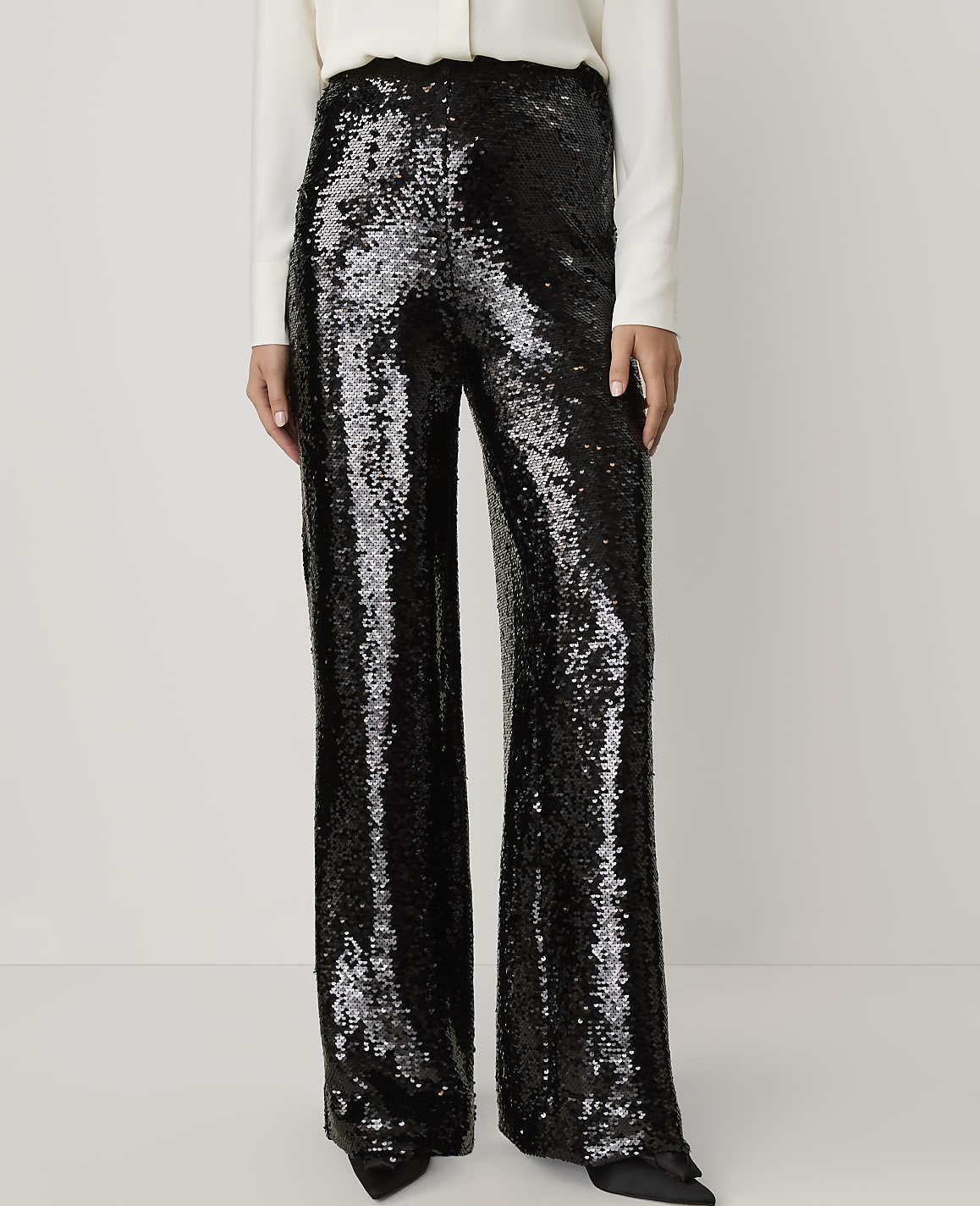 A person wears shimmering black sequined wide-leg trousers and a white top against a plain, light-colored background.