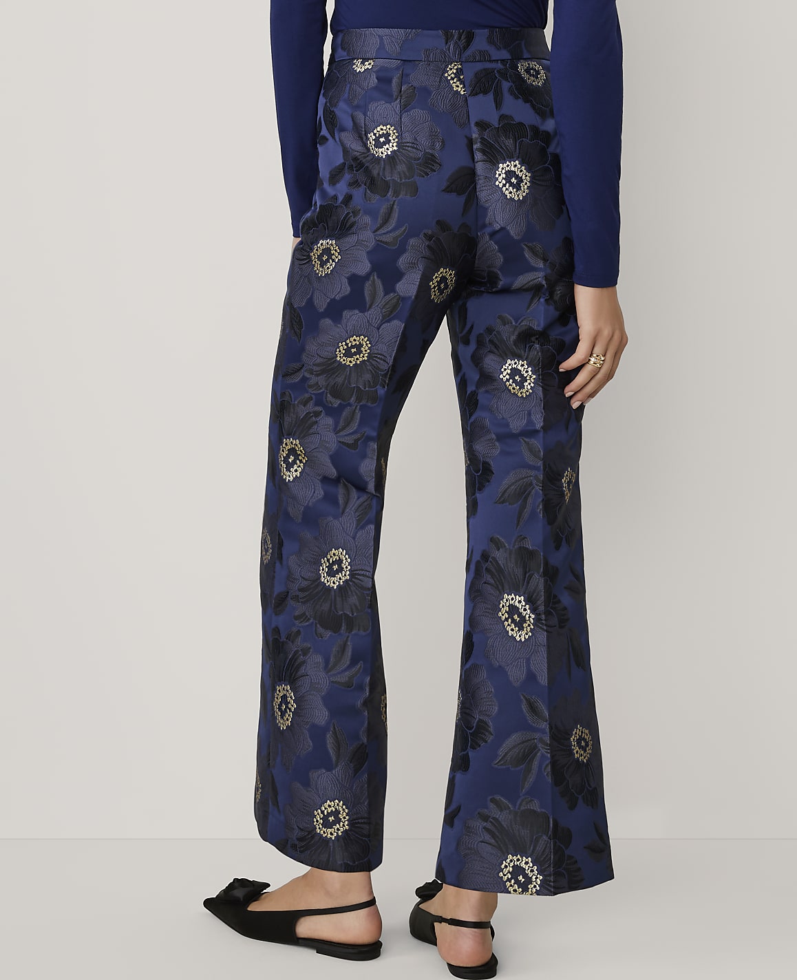 A person wears navy blue floral patterned trousers and black bow-accented sandals against a plain white background.