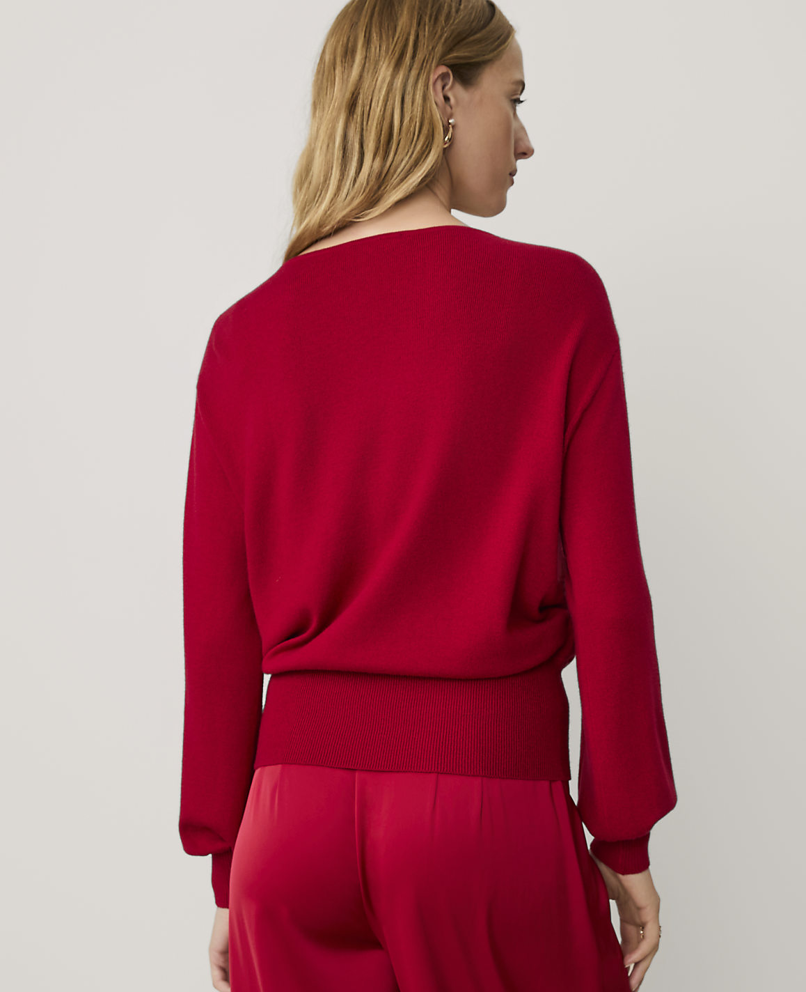 A woman wearing a red sweater and matching red pants stands against a plain, light-colored background.