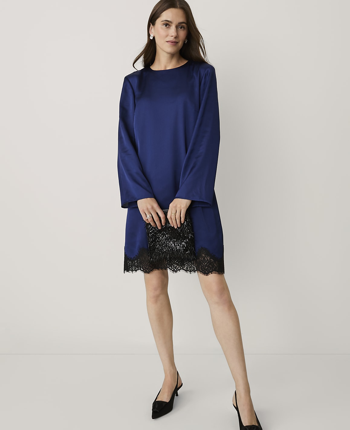 A woman wearing a royal blue satin dress with black lace trim and black heels stands against a plain white background.