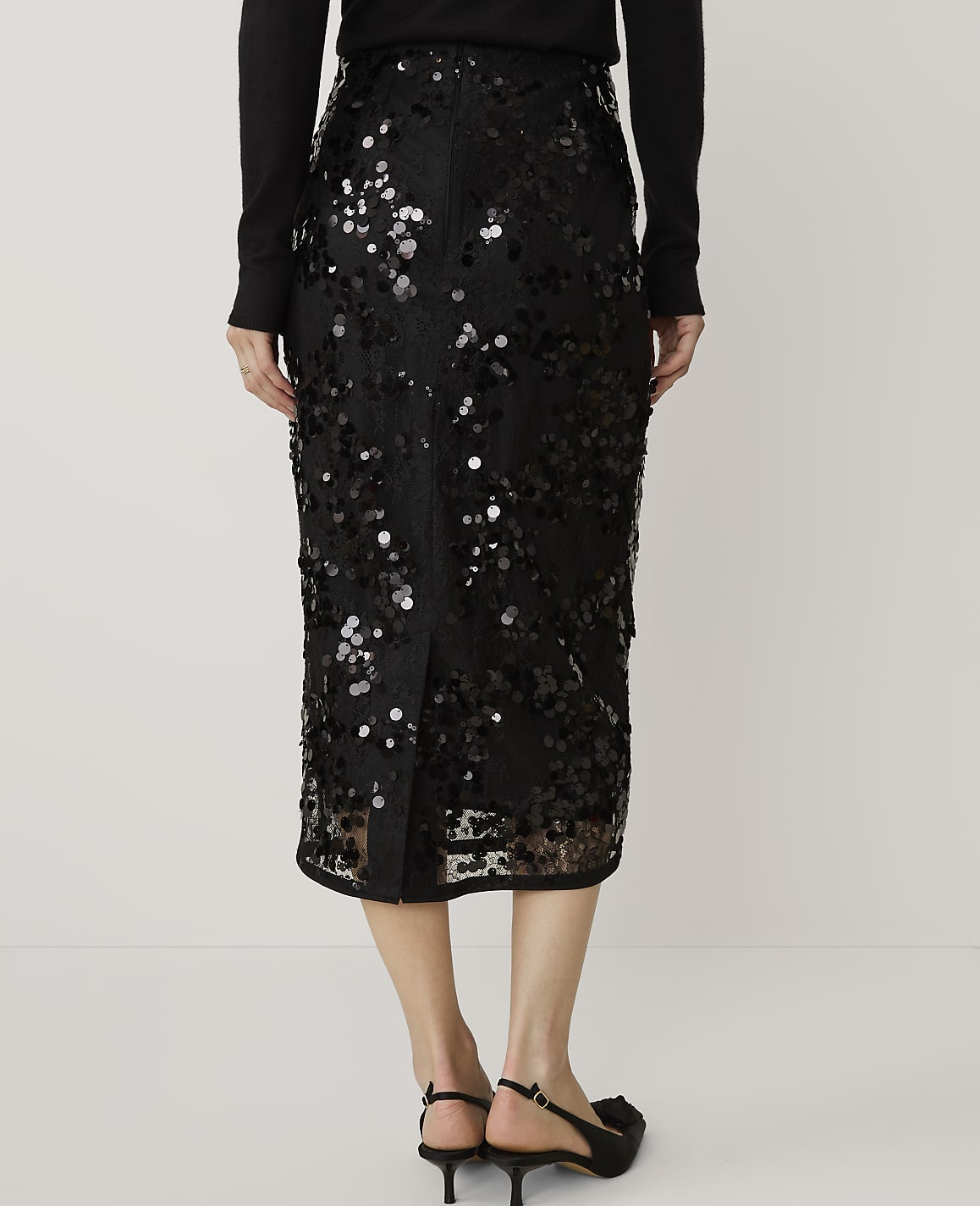 A person wearing a black sequined midi skirt and black heels stands against a plain white background.