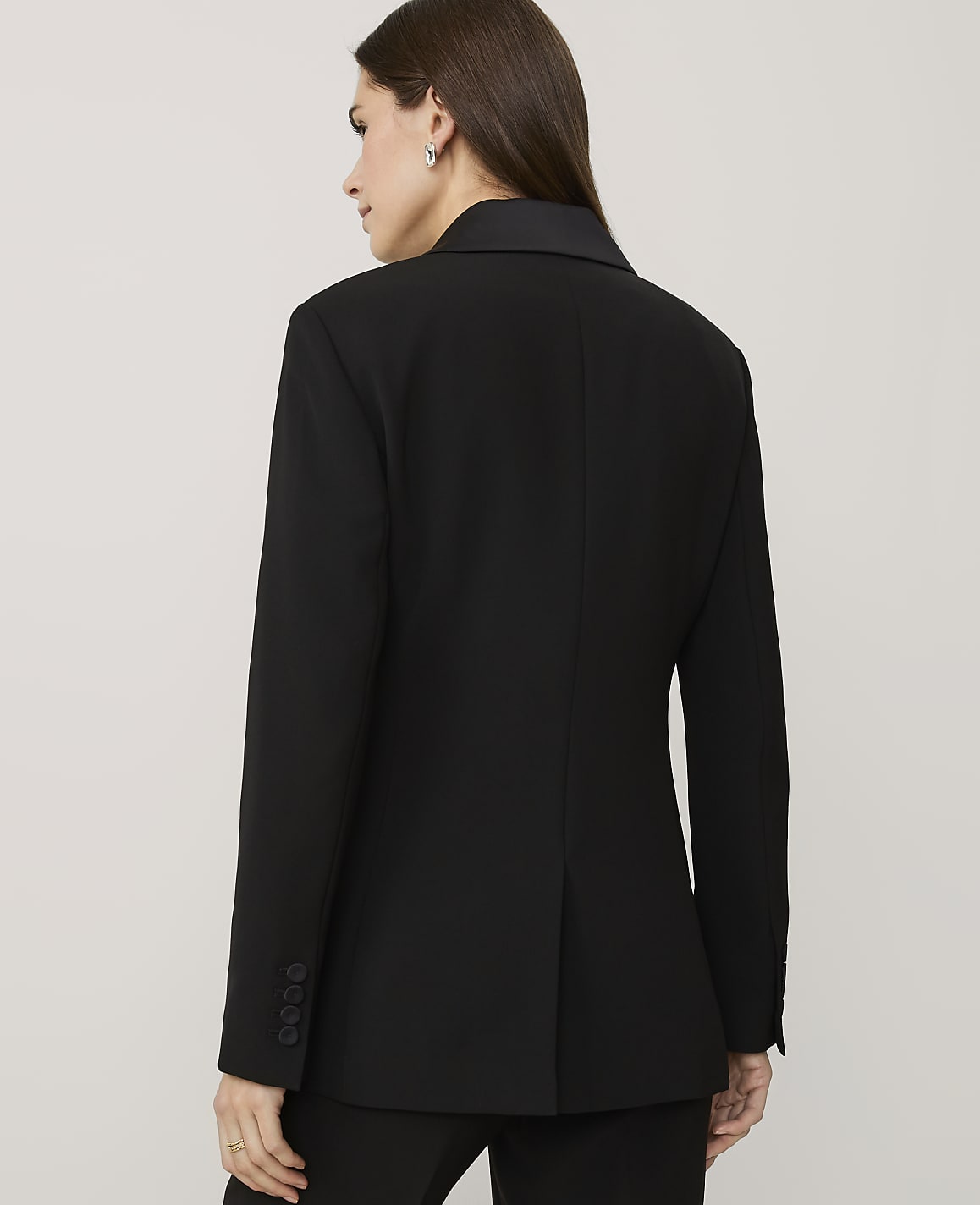 A woman wearing a black blazer is seen from behind against a plain, light-colored background.