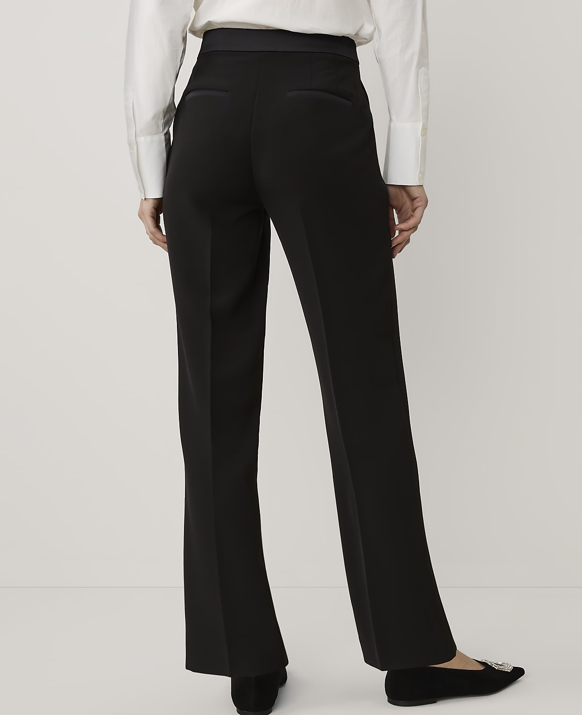 A person wearing a white shirt and black trousers stands against a plain white background.