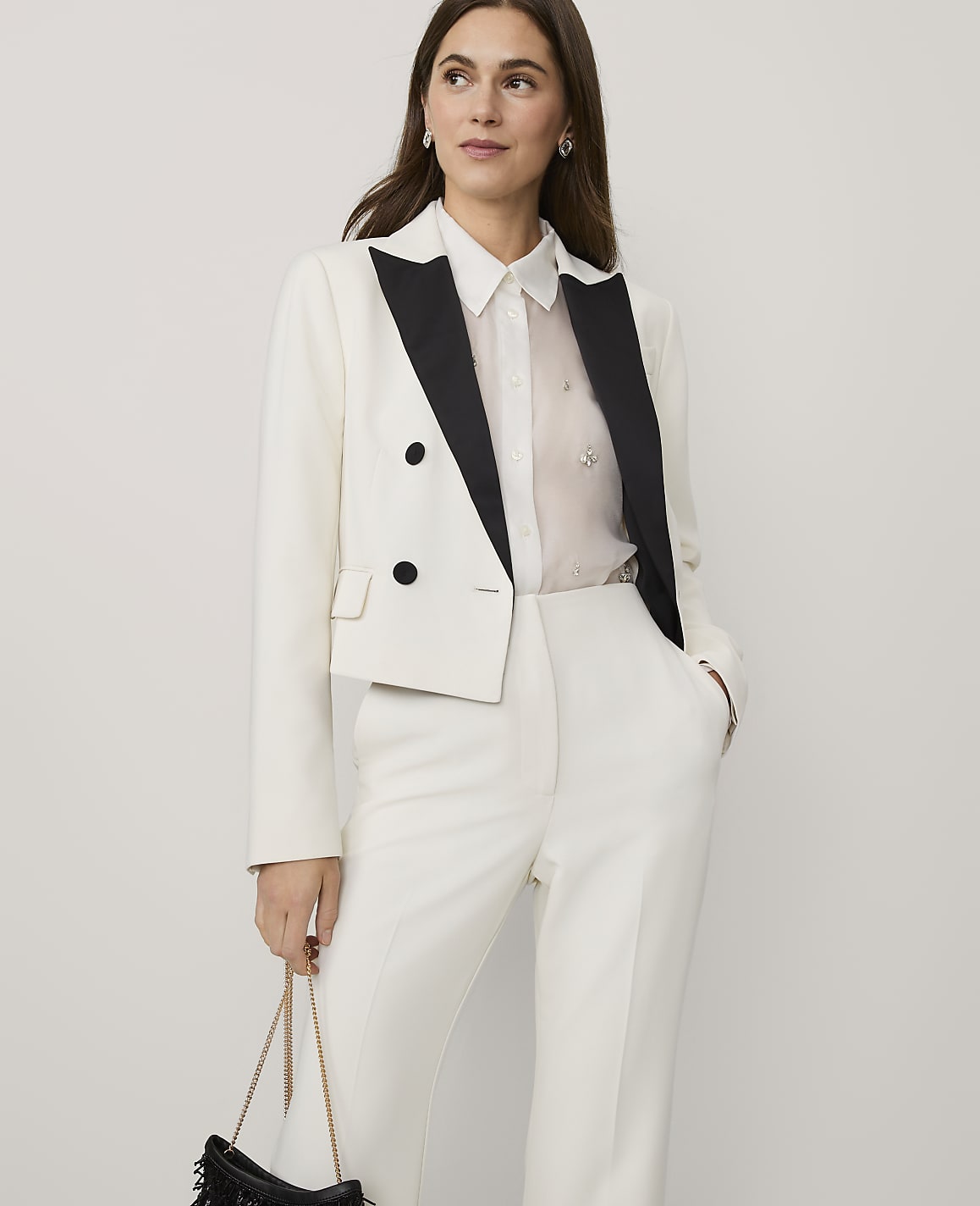 A woman wearing a white cropped blazer and matching trousers stands against a plain, light-colored background.