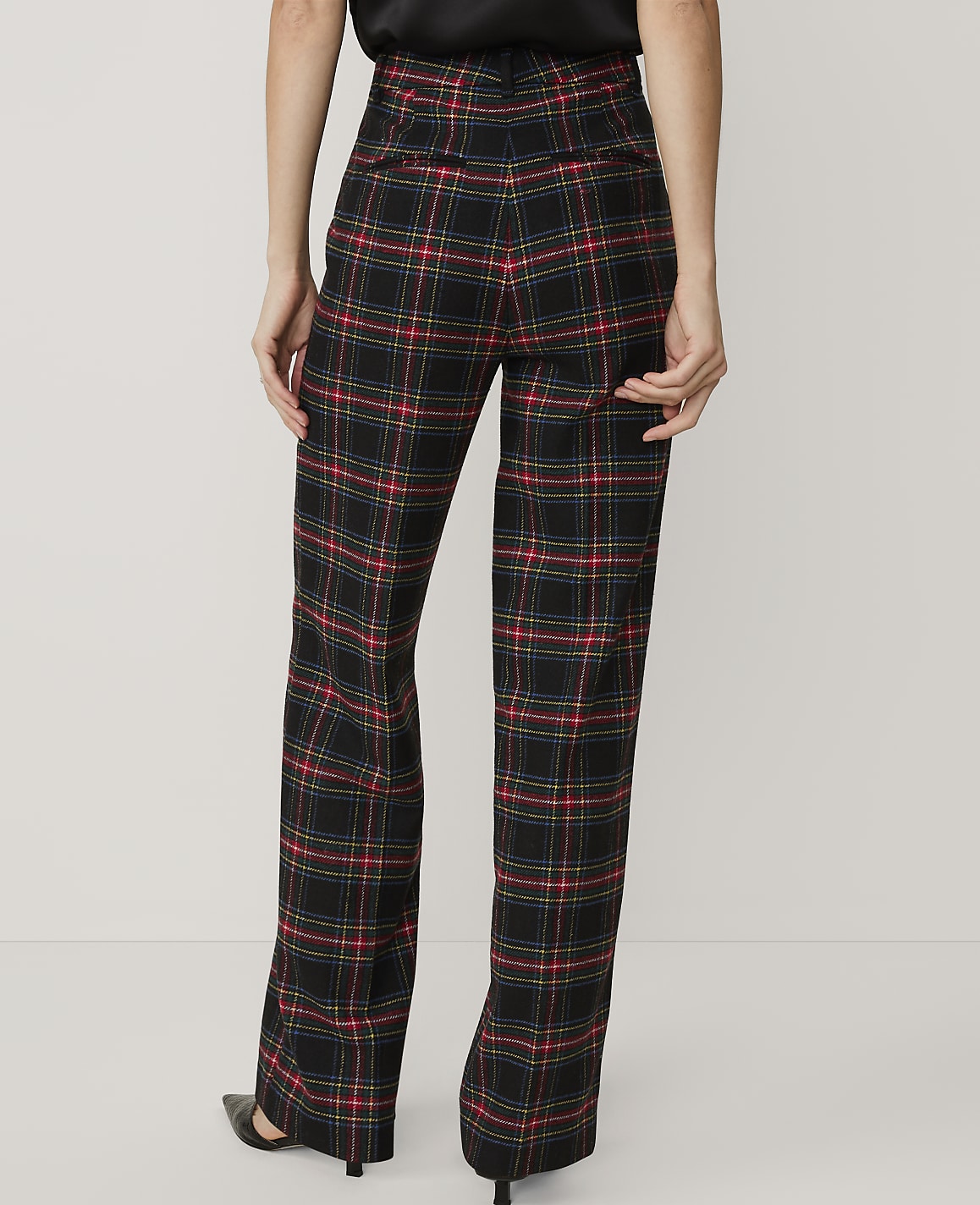 A person wearing black, red, and blue plaid trousers and black heels stands against a plain white background.