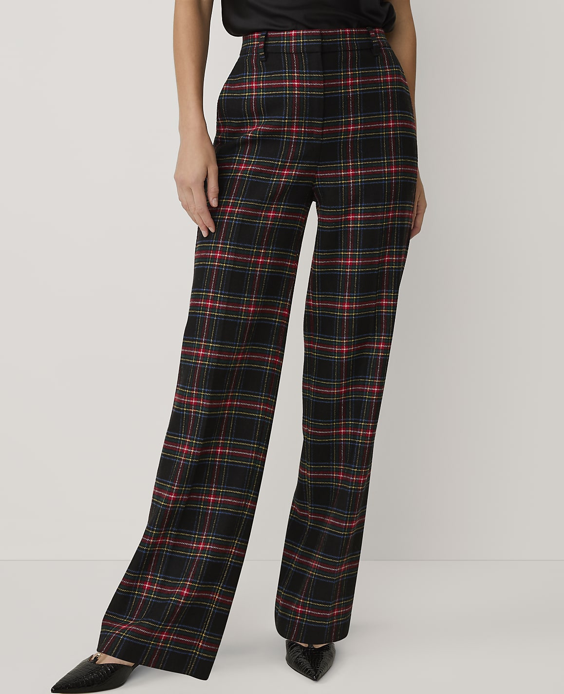 A person wears black, red, and yellow plaid wide-leg trousers and black pointed shoes against a plain white background.