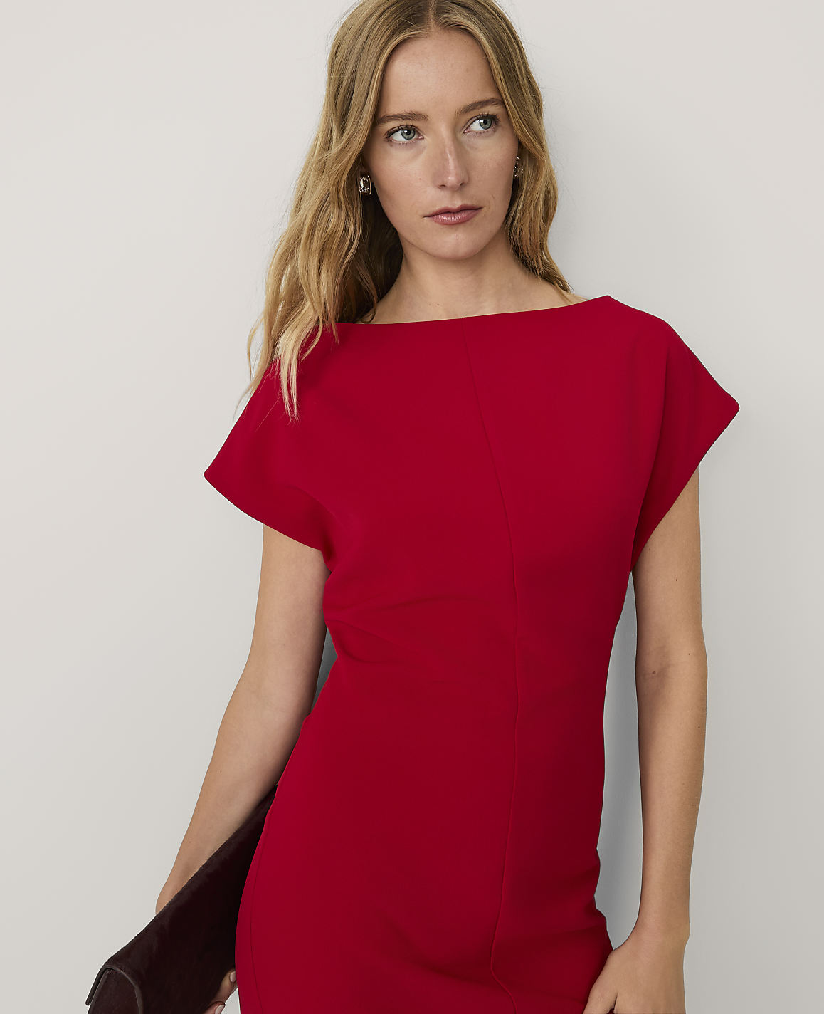A blonde woman wearing a red short-sleeved dress stands against a plain white background.