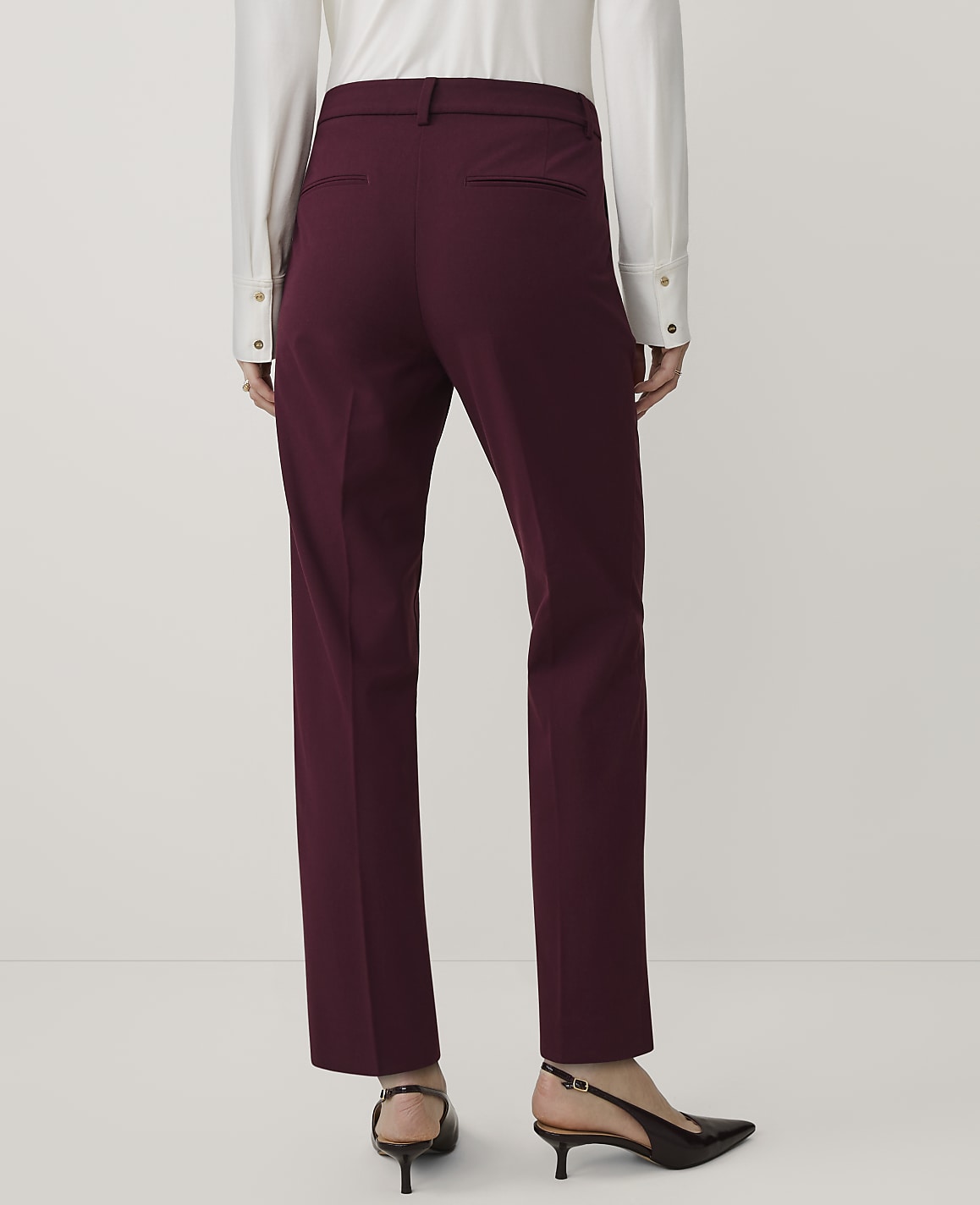 A person wearing a white shirt and burgundy trousers stands against a plain white background.