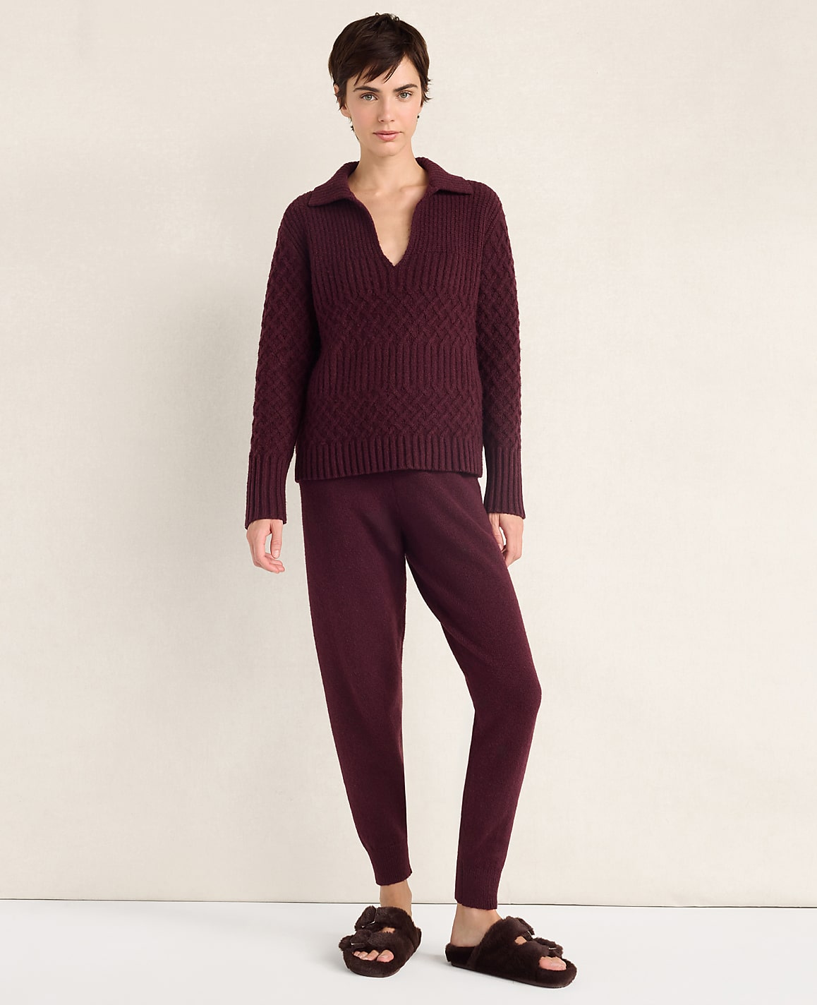 A woman wearing a burgundy knit sweater and matching pants stands against a plain, light-colored background.