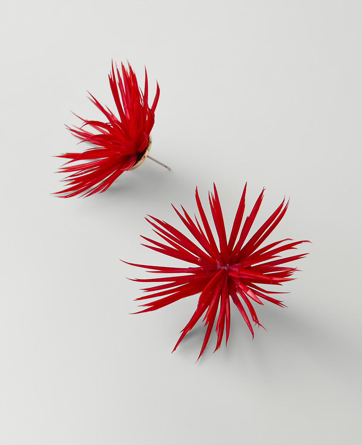 Two vibrant red, spiky floral ornaments rest on a plain, light gray background.