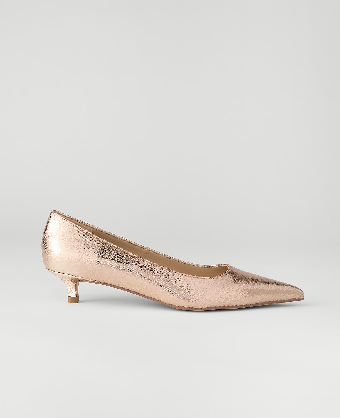 A metallic rose-gold pointed-toe pump sits in the foreground against a plain, light gray background.