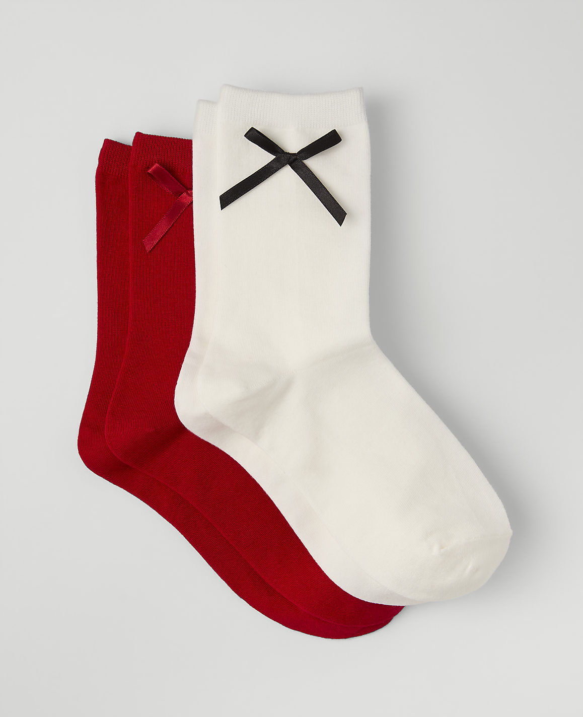 Three socks, one white and two red, each adorned with a small bow, are layered on a plain light gray background.