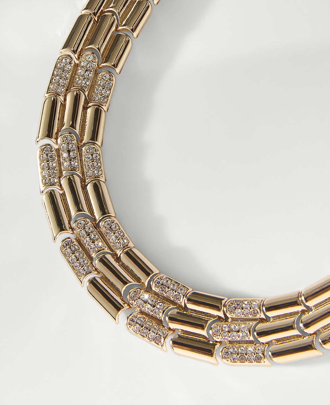 A gold-toned chain with sparkling diamond-encrusted links curves across a plain white background.