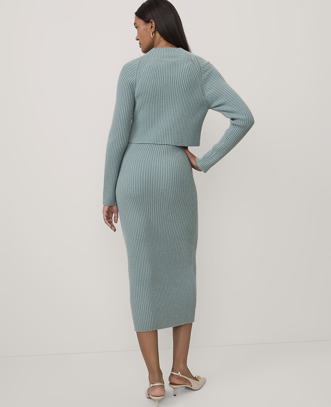 A woman stands with her back to the camera wearing a sage green ribbed knit two-piece set against a plain white background.