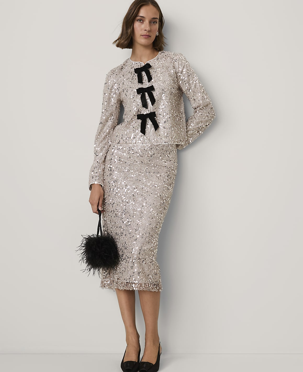 A woman wearing a shimmering champagne sequin jacket and matching skirt stands against a plain white background.
