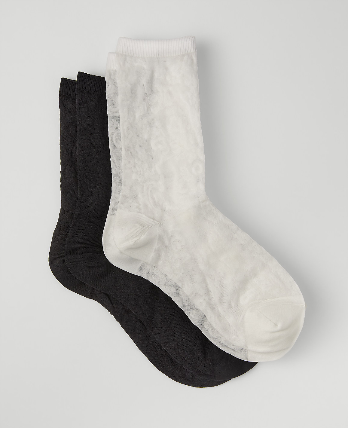 A white sock rests on top of two black socks against a plain light gray background.