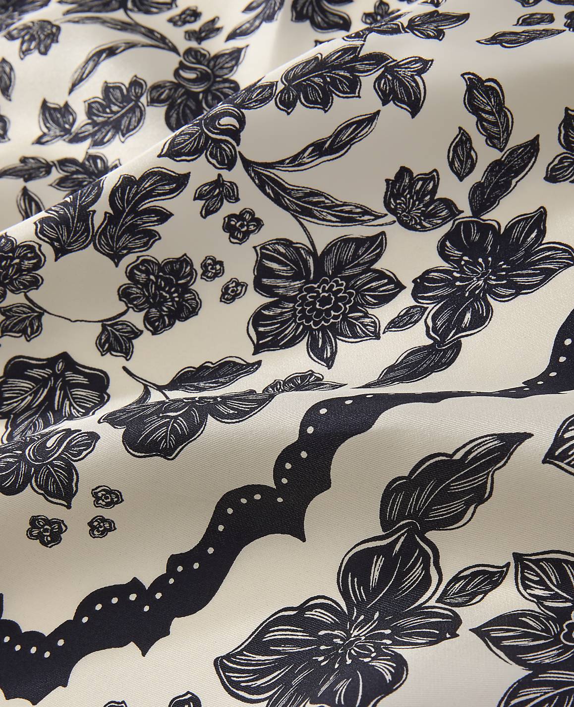 Dark navy floral patterns and scalloped borders are printed across a draped, off-white fabric.