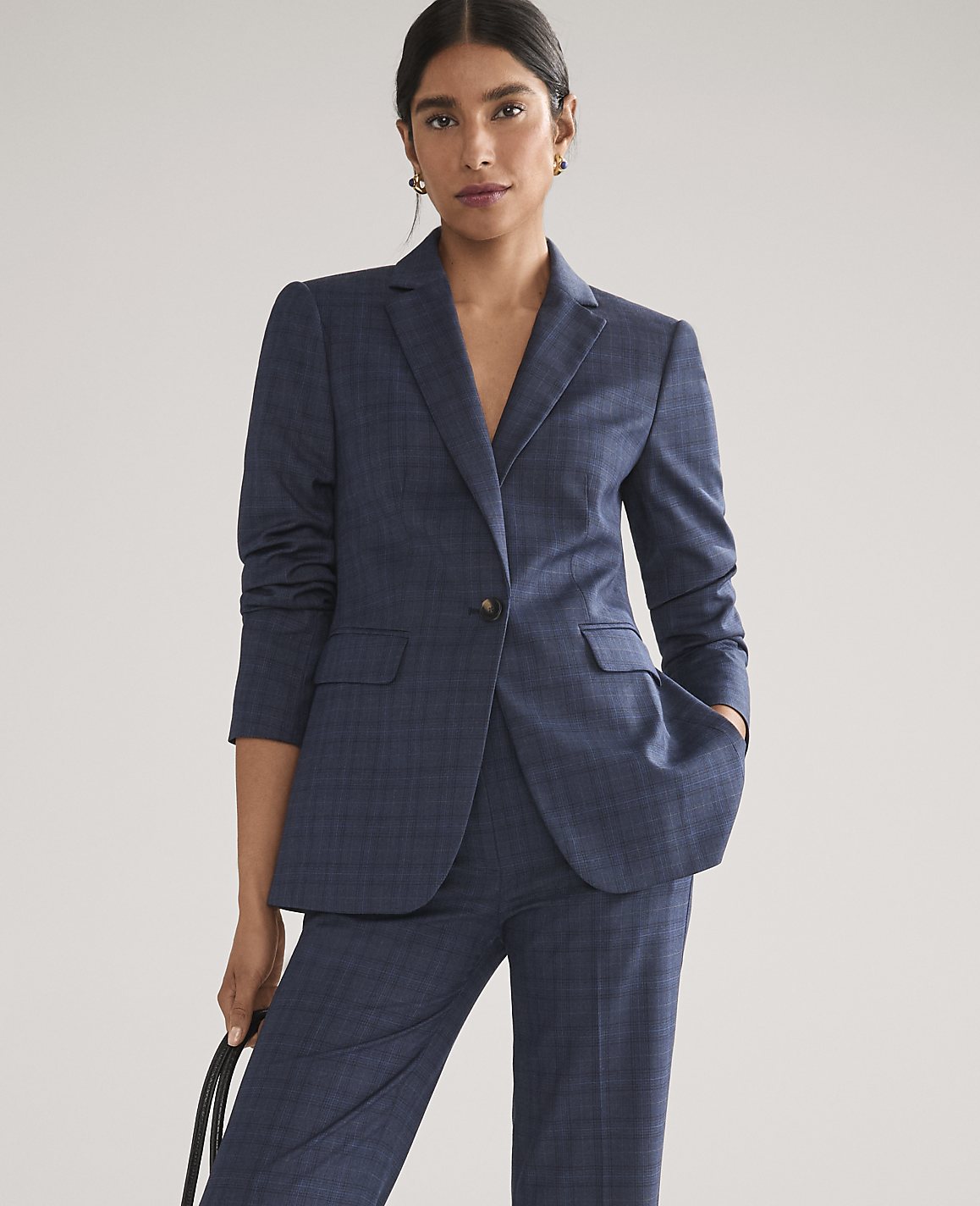 A woman wearing a navy blue plaid suit stands against a plain, light gray background.