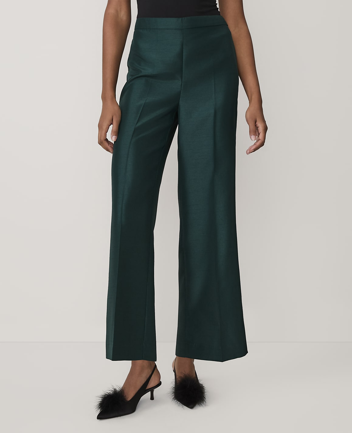 A person wearing dark green wide-leg trousers and black feathered heels stands against a plain white background.