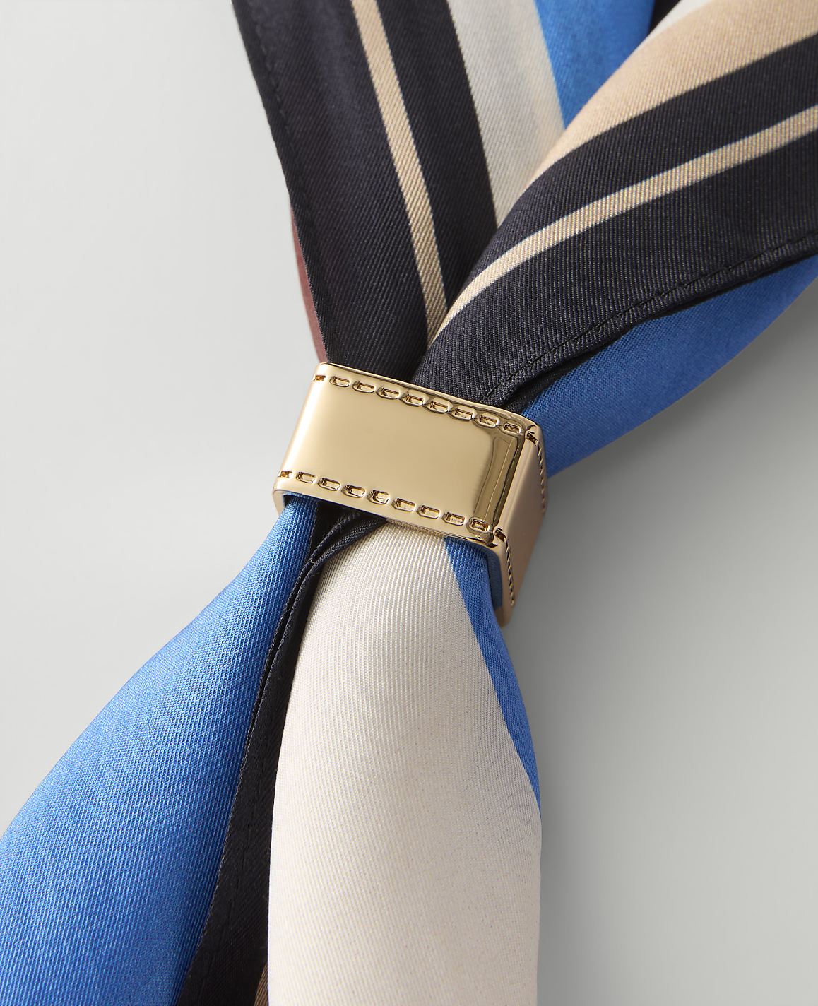 A gold-toned square ring with film strip perforations sits centered on a plain light gray background.