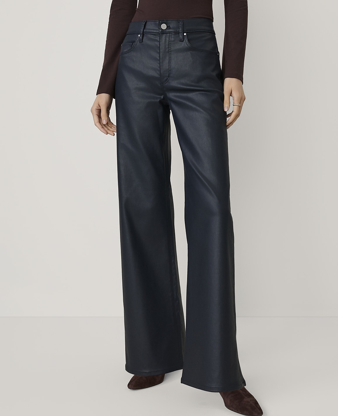A person wears wide-leg navy faux-leather trousers and a dark burgundy top against a plain, light-colored background.
