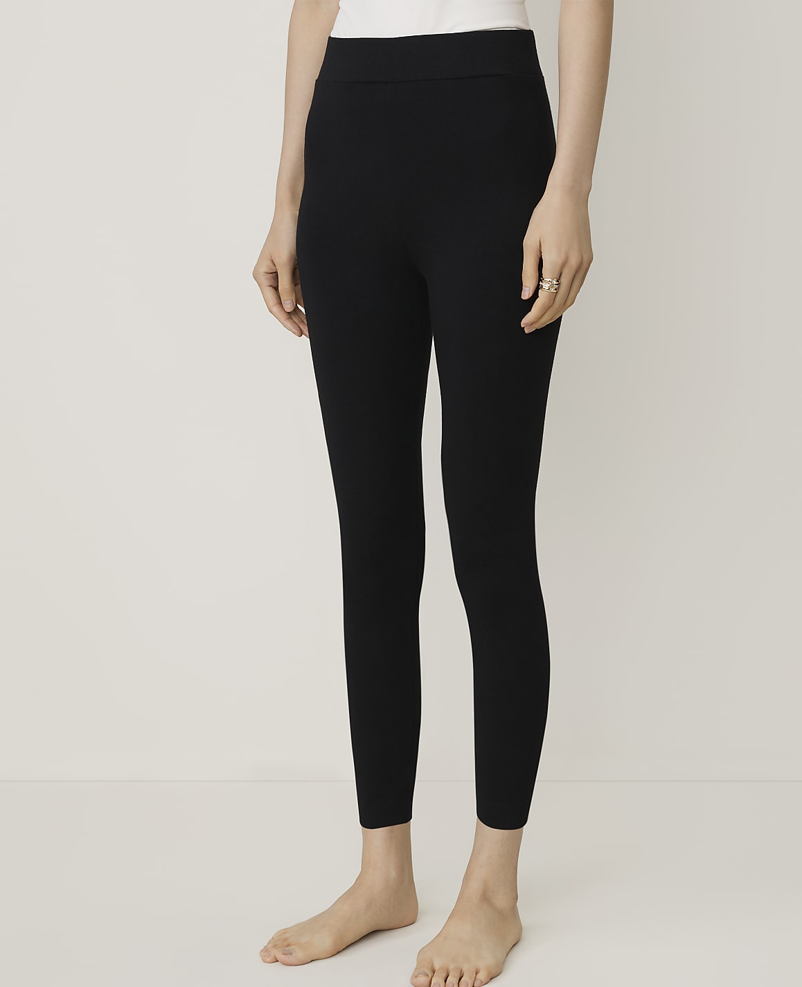 A person wearing black leggings and a white top stands against a plain, light-colored background.