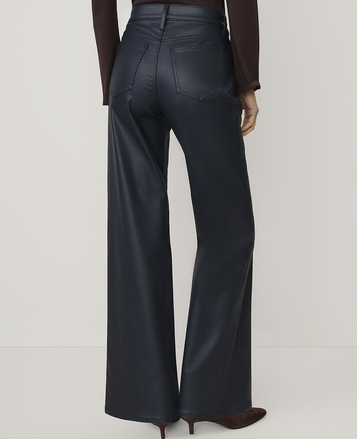 A person wearing dark navy wide-leg faux leather trousers and a burgundy top stands against a plain white background.
