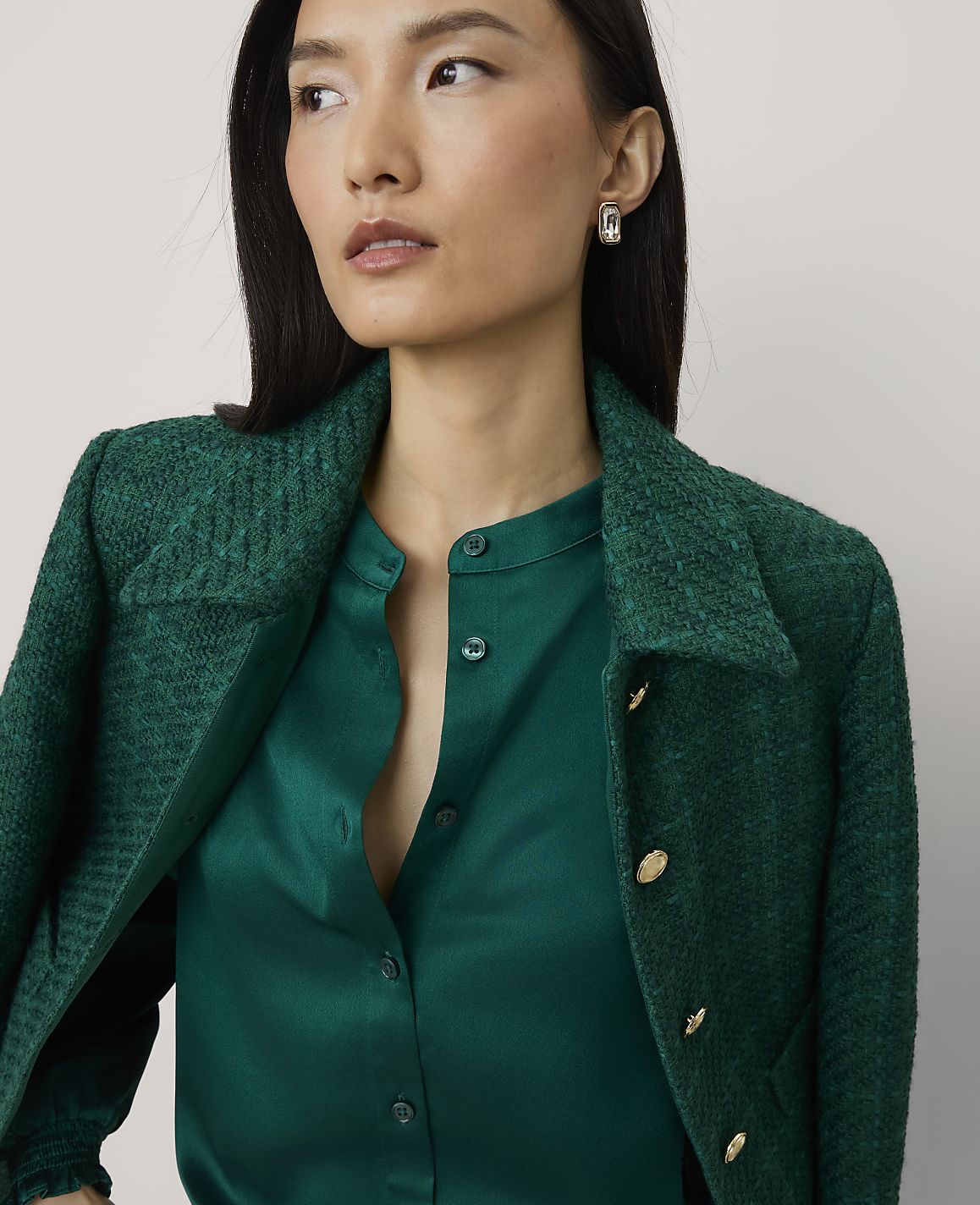 A woman wearing a green satin shirt and a matching green textured blazer stands against a plain, light-colored background.